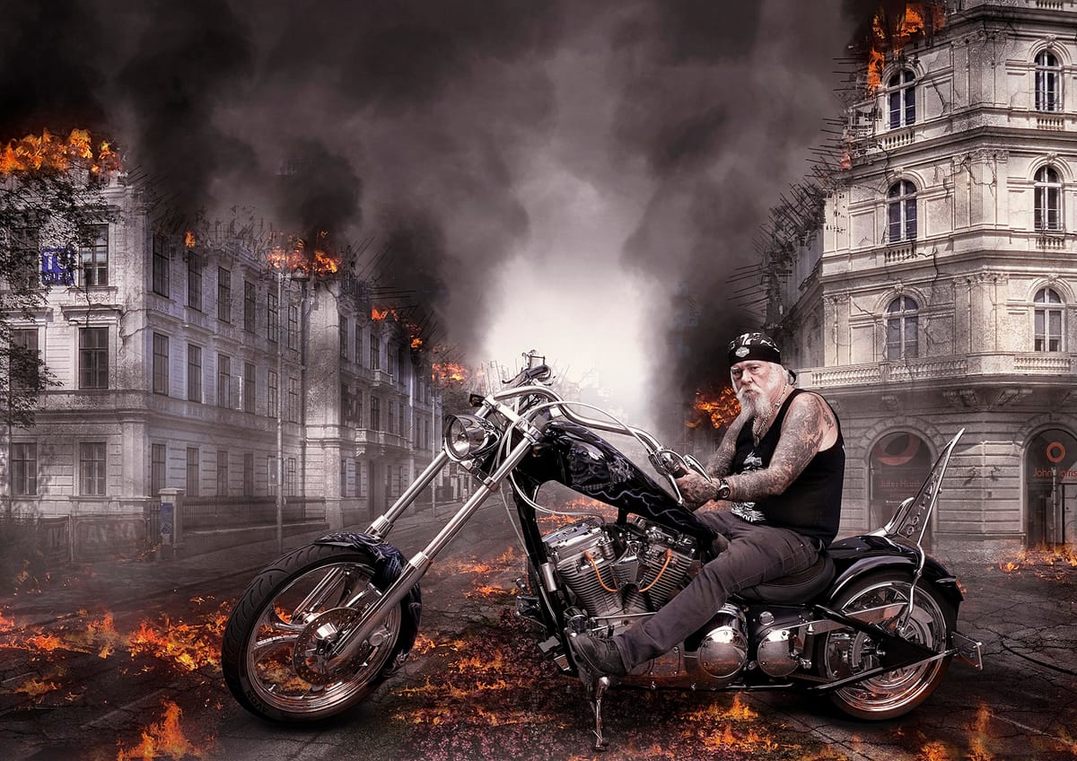 Tattoo Artist Tony Cohen in his chopper motorbike with a burning city behind him